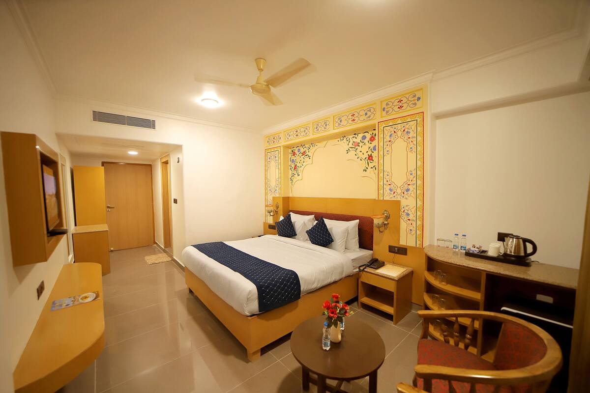 Hotelkamer met een bed, bureau, stoel, een klein tafeltje met bloemen en een plafondventilator.