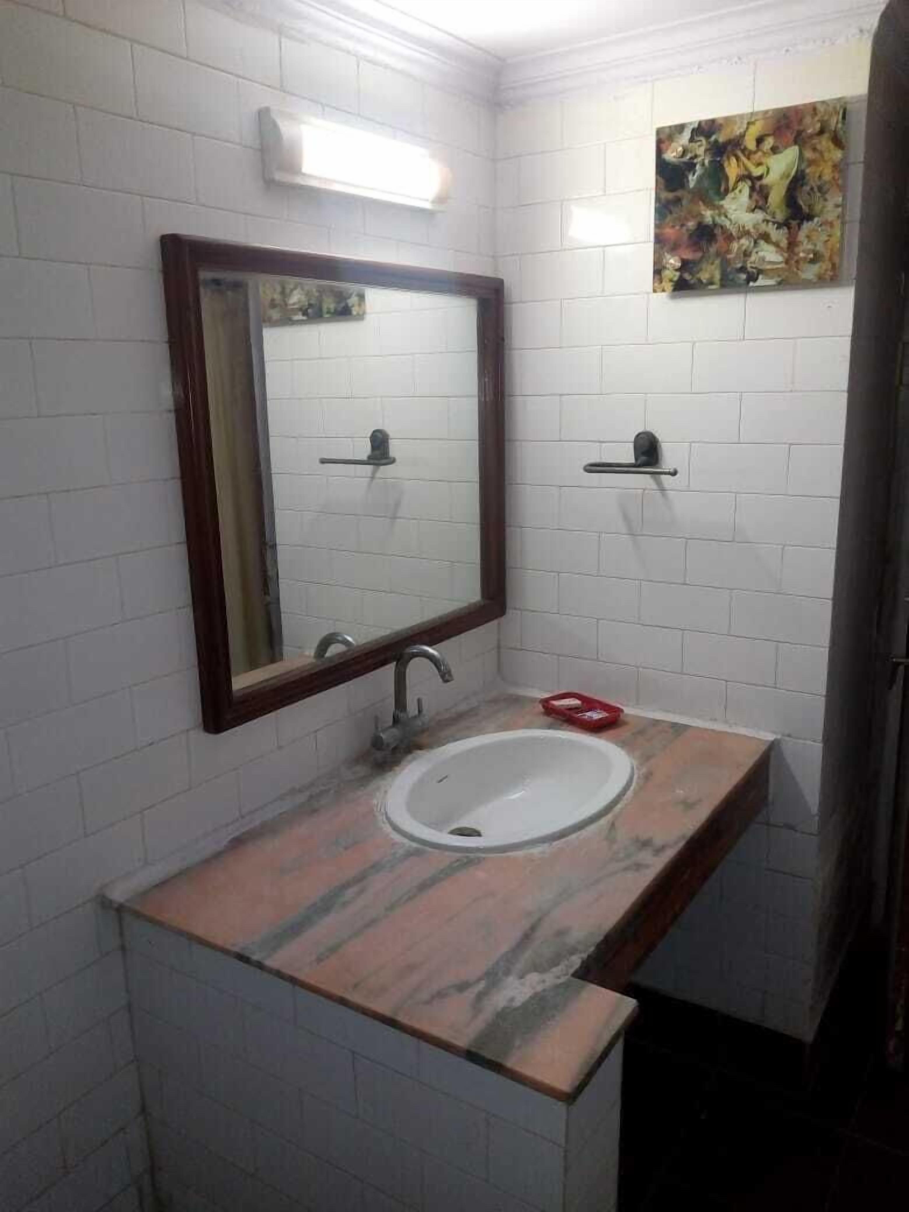 A bathroom with a white tiled wall, a marble countertop, a sink, a mirror, and a shelf with a red object.
