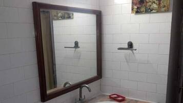 A bathroom with a white tiled wall, a marble countertop, a sink, a mirror, and a shelf with a red object.