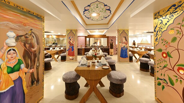 Un restaurante con decoración tradicional, que incluye murales y un área central de comedor con mesas redondas y taburetes.
