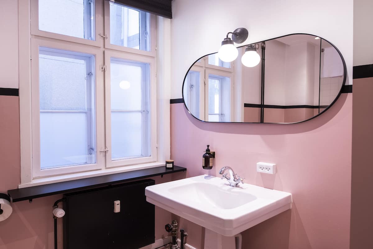Une salle de bain avec un lavabo blanc, un miroir rond et une fenêtre à quatre carreaux.