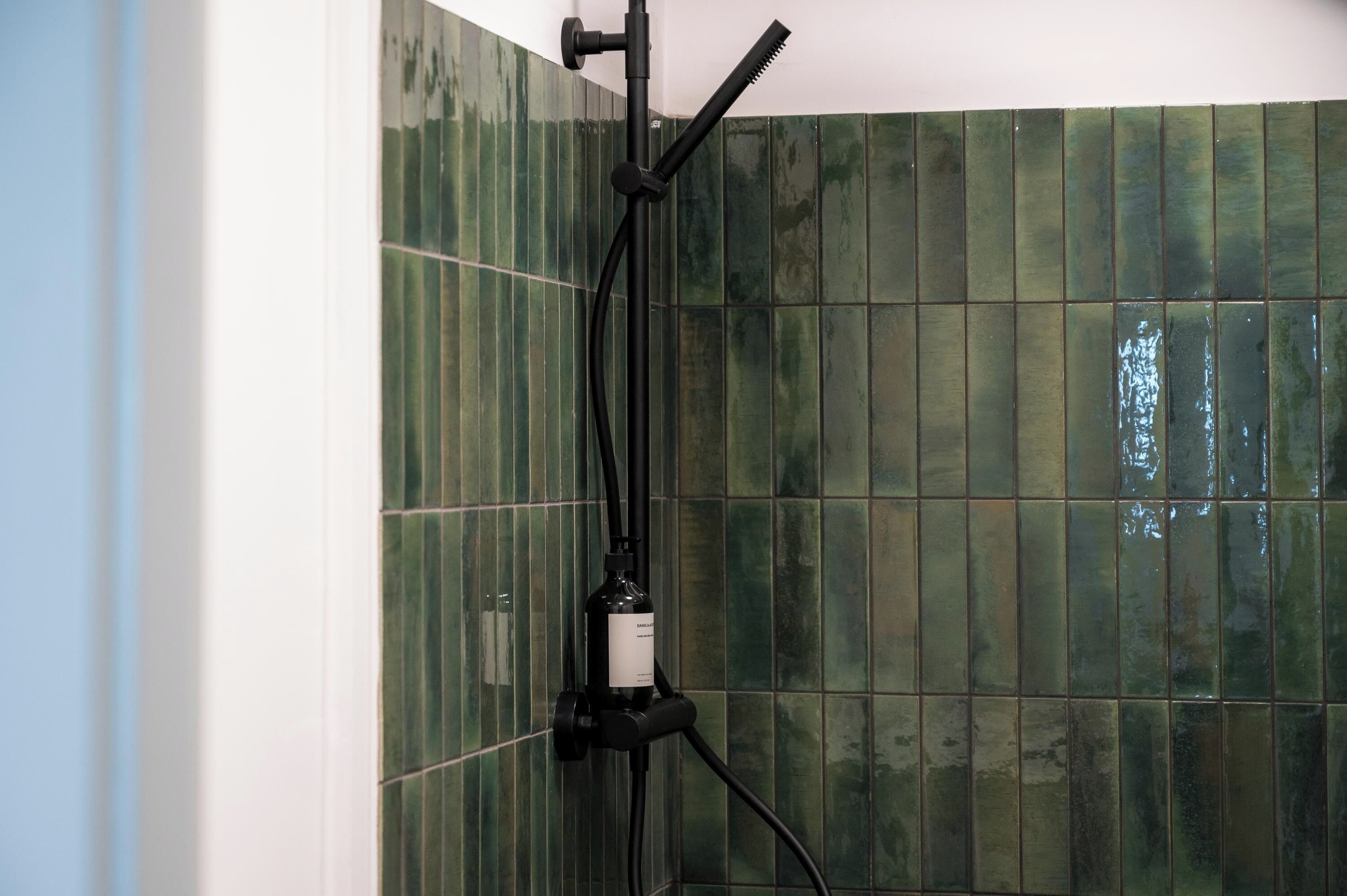 A bathroom with green tiled walls and a black showerhead.