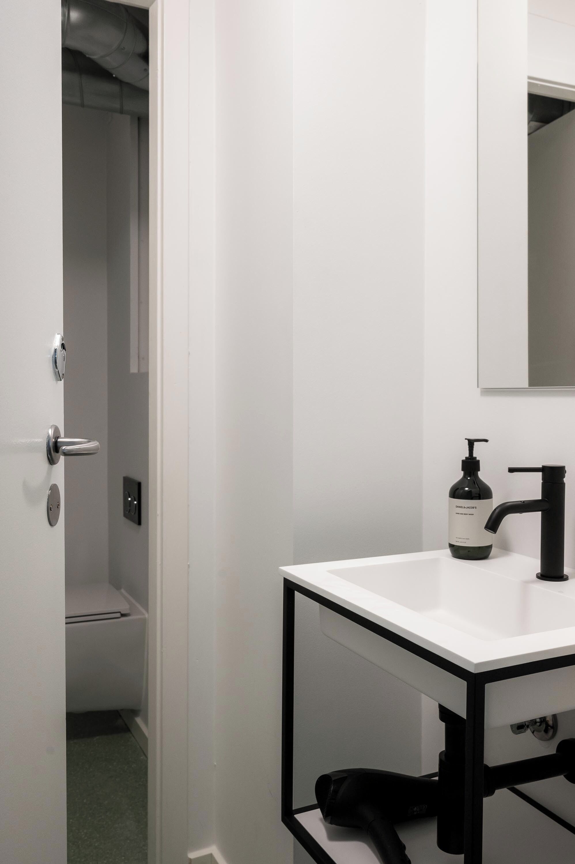 Une salle de bain avec un lavabo blanc, un robinet noir et un flacon de savon pour les mains.