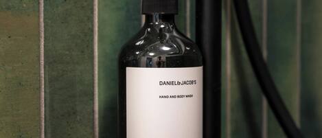 A bottle of Daniel & Jacob's Hand and Body Wash on a black soap dish against a green tiled wall.