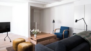 A modern living room with a flat-screen TV, a wooden coffee table, a blue armchair, and a sofa.