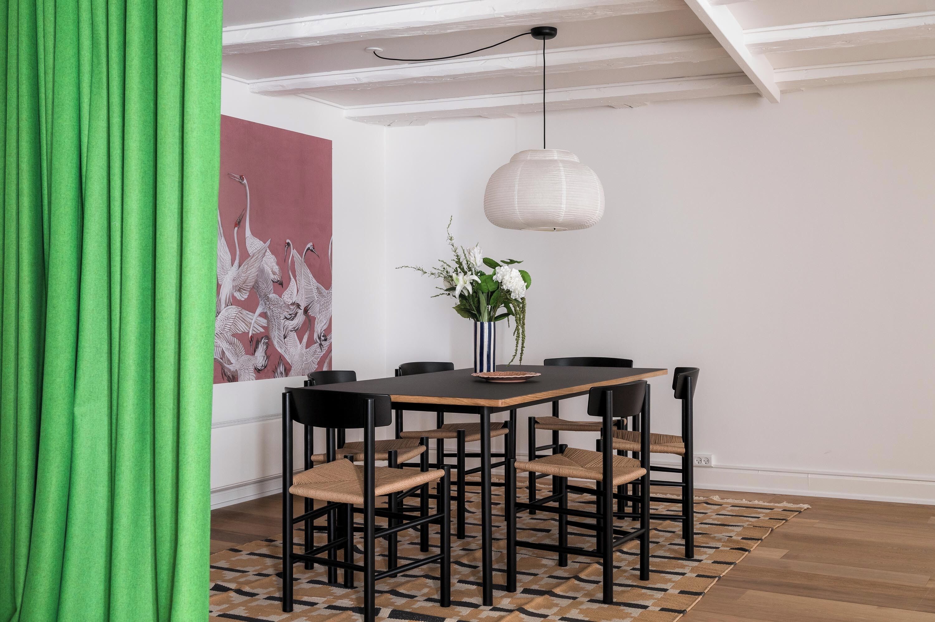 A dining area with a wooden table, black chairs, a white pendant light, and a vase with flowers.