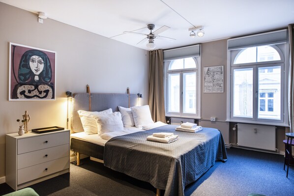 Ein Hotelzimmer mit einem Bett, einem Nachttisch, einem Deckenventilator und großen Fenstern.