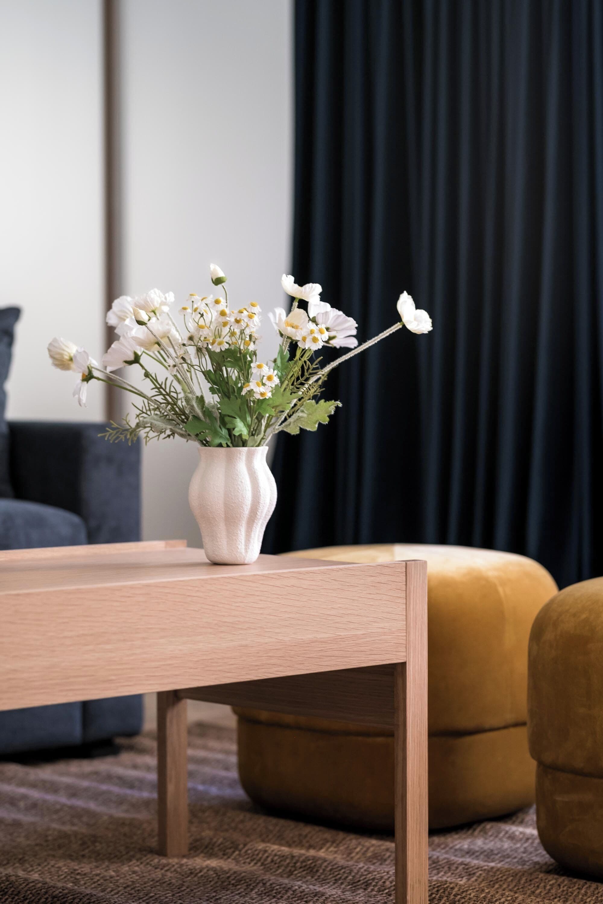 Eine weiße Vase mit Blumen auf einem Holztisch in einem Wohnzimmer.