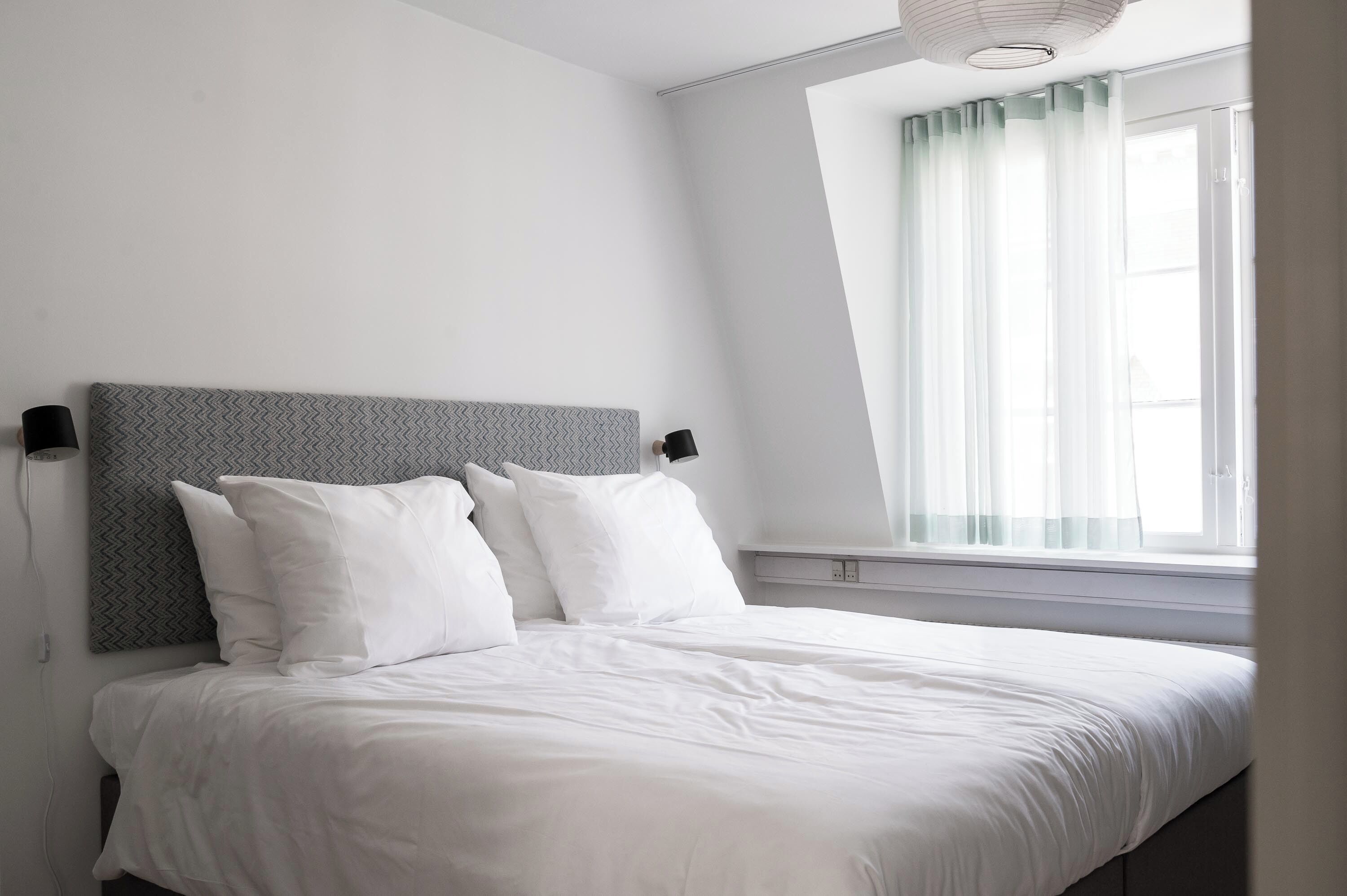 A neatly made bed with white linens, a grey patterned headboard, and two bedside lamps.