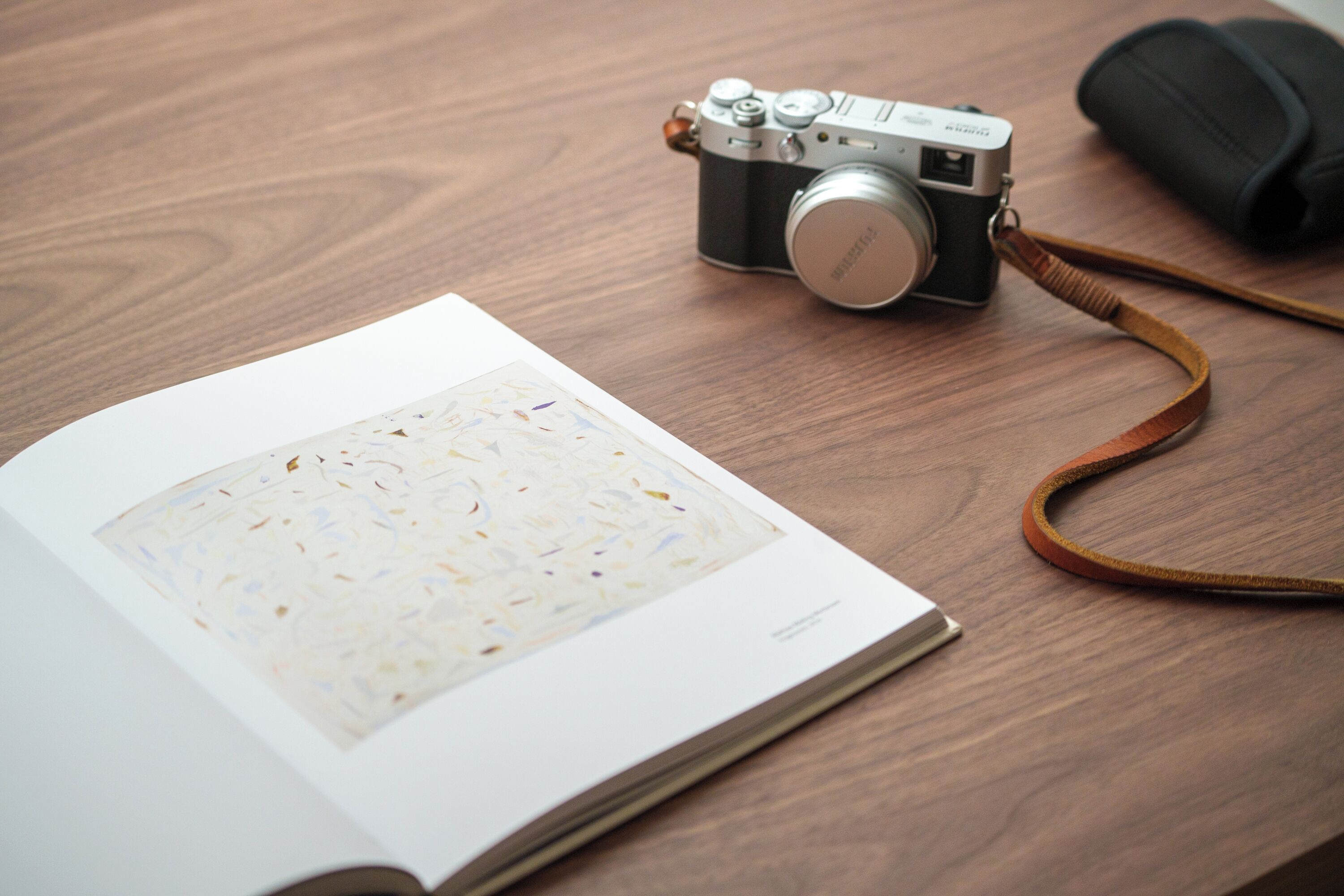 A camera on a wooden table with a book and a rolled-up item beside it.
