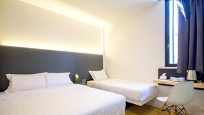 Quarto de hotel com duas camas de solteiro, uma escrivaninha com cadeira e uma janela com cortinas.