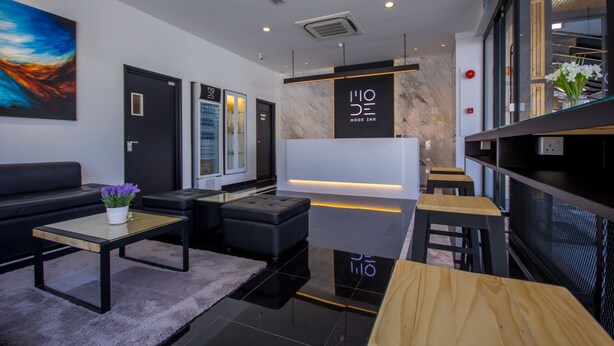 Um hall de hotel moderno com um sofá preto, uma mesa de centro de madeira, um banquinho preto e um balcão de recepção.