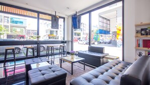 Um interior moderno com sofá, poltronas e uma mesa pequena. Janelas amplas oferecem vista para a rua.