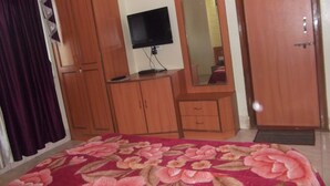 A bedroom with a bed, wooden wardrobe, a television, and a mirror. - Hotel Ravikant (Pune)