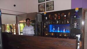 A bar area with a wooden counter and shelves of bottles. - Hotel Ravikant (Pune)