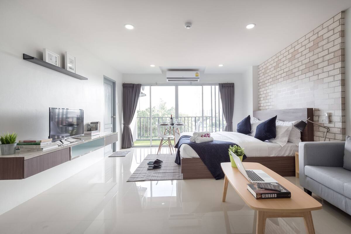 A modern hotel room with a bed, a sofa, a TV, a desk, and a balcony with a view.