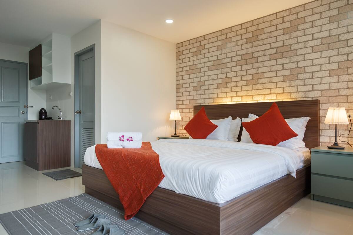 A modern hotel room with a brick wall, a wooden bed frame, white bedding, and two nightstands with lamps.