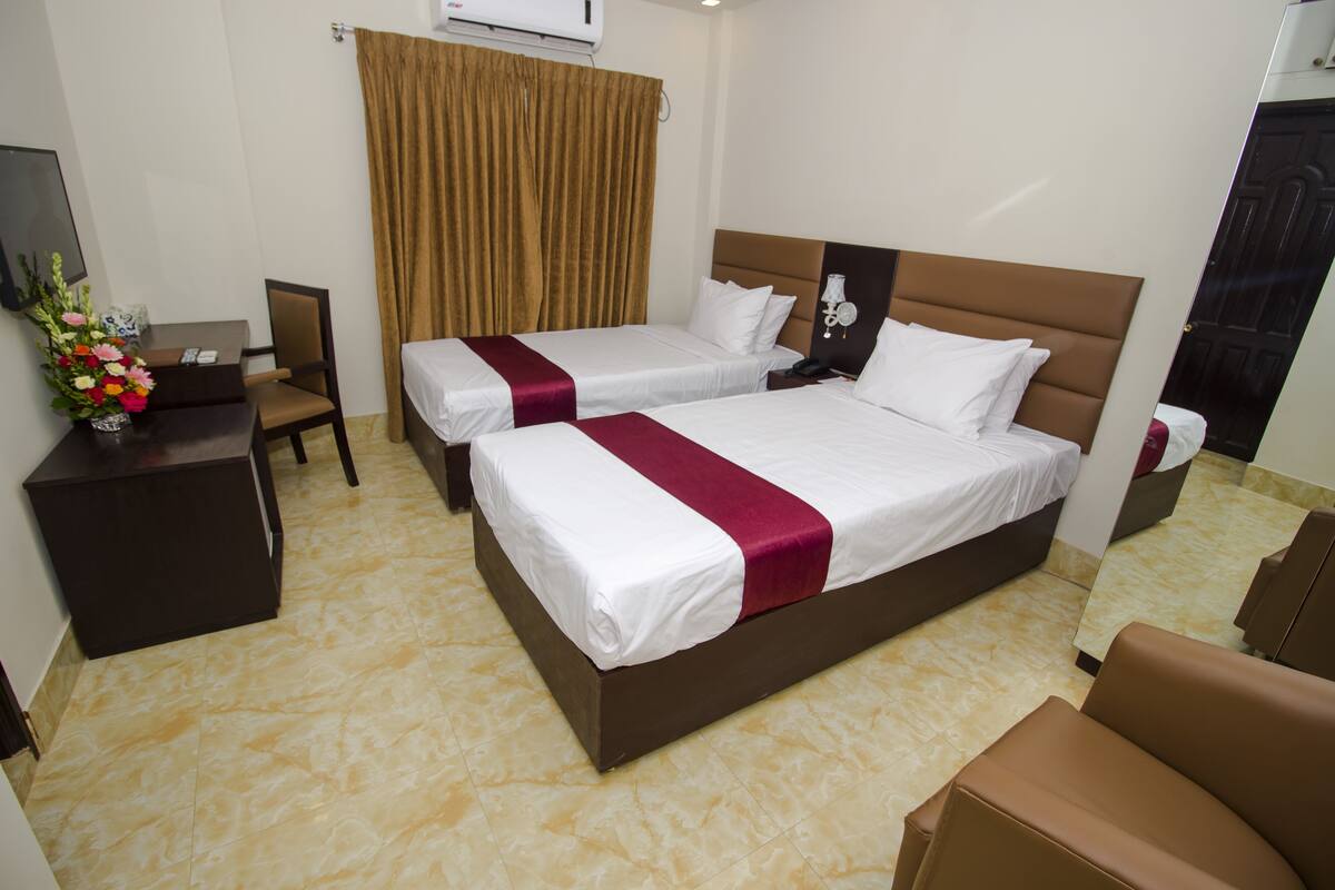 A hotel room with two beds, a desk, a chair, and a mirror.