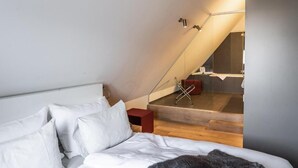 Un dormitorio con cama, una mesita de noche roja y una escalera que lleva a un baño con bañera.