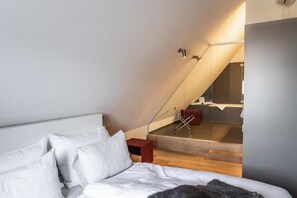 A bedroom with a bed, a red nightstand, and a staircase leading to a bathroom with a bathtub.