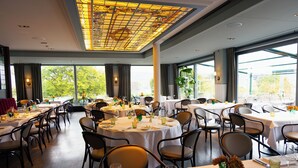 Un restaurante con mesas redondas, sillas y un amplio techo de vitrales.
