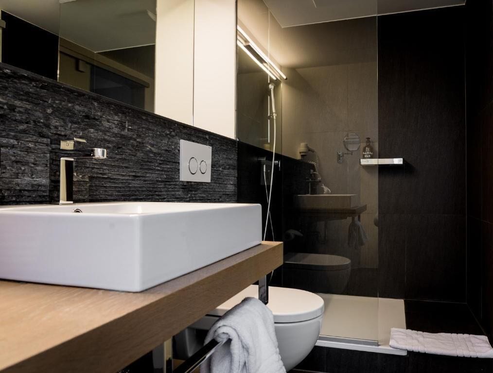 A modern bathroom with a white sink, a mirror, a shower, and a toilet.