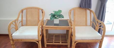 Two wicker chairs with white cushions and a small table with a plant between them.