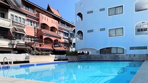Une piscine dont le bord est revêtu de carreaux, entourée d’immeubles dotés de balcons et d’une enseigne indiquant la présence d’une laverie.