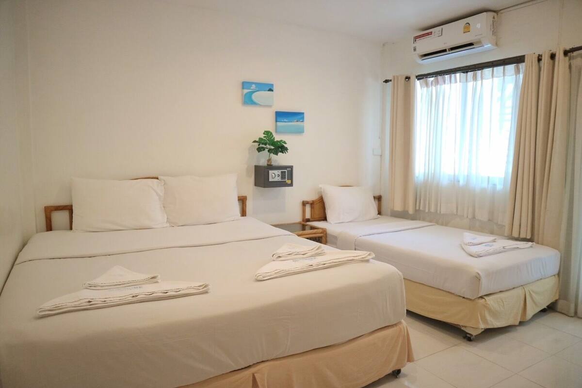 Habitación de hotel con dos camas, una mesita con una planta y una ventana con cortinas.