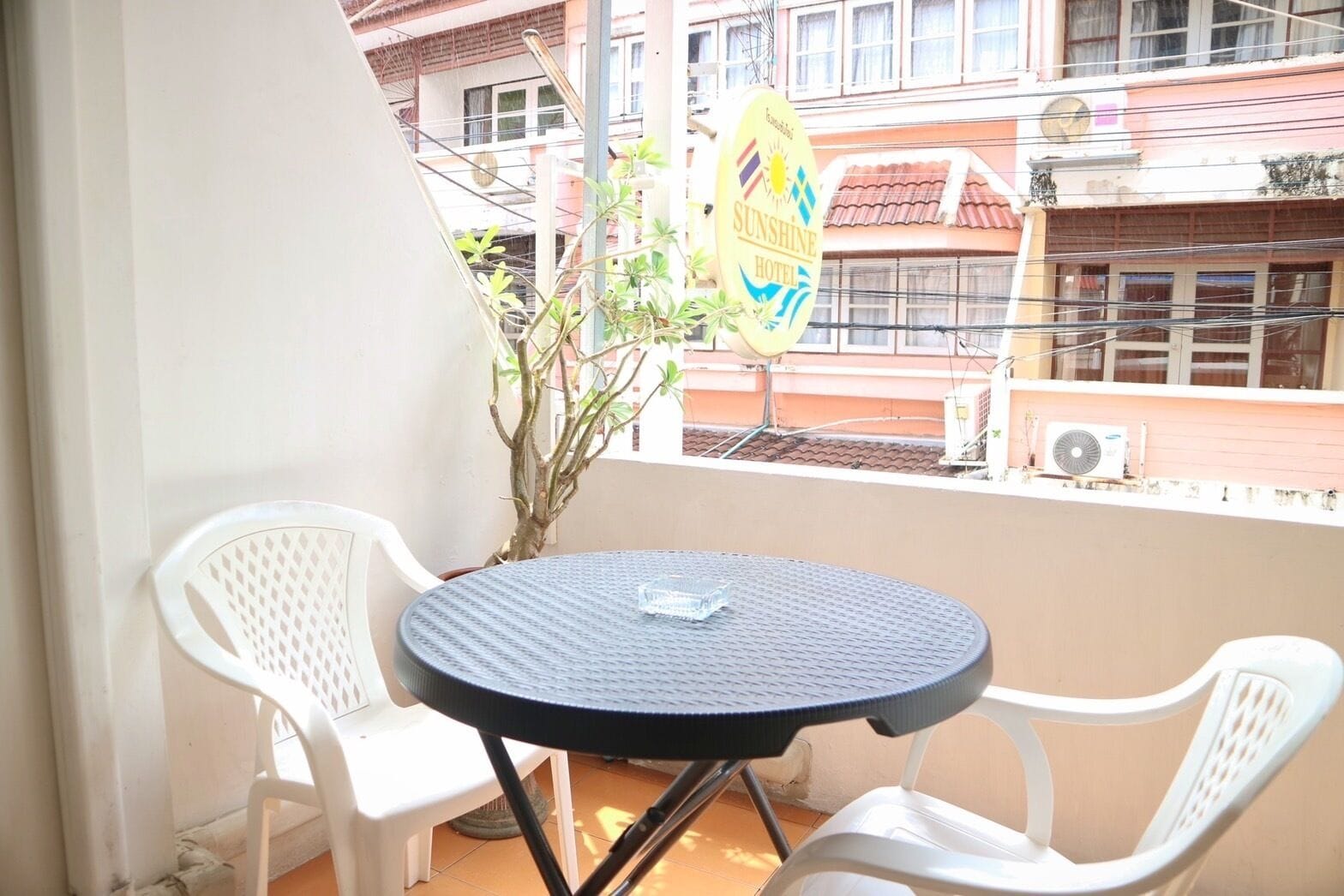 A balcony with a round table and two white chairs, a potted plant, and a sign for Sunshine Hotel.