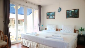 Une chambre d’hôtel avec un grand lit, une chaise en bois, une table de chevet et une vue sur l’extérieur grâce à une porte-fenêtre coulissante.