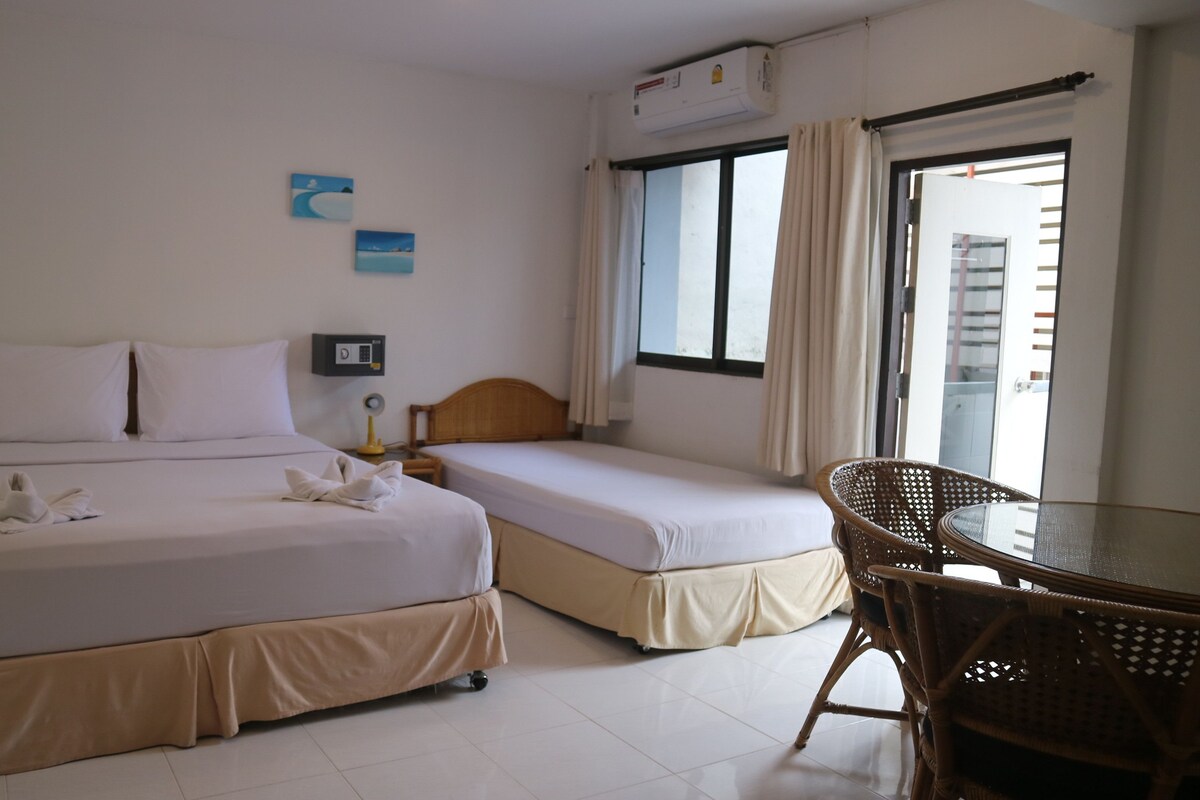 Une chambre d’hôtel avec deux lits, une petite table, une chaise, un appareil de climatisation et une fenêtre avec des rideaux.