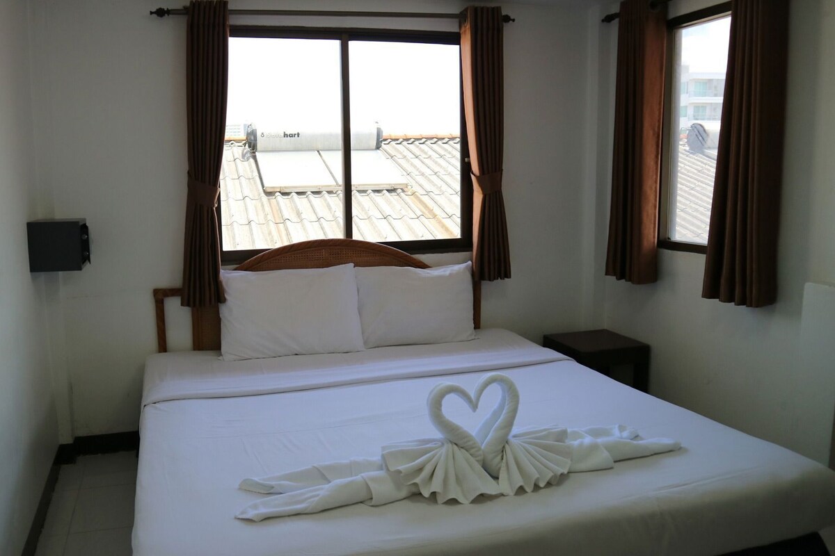 Quarto de hotel com cama, janela, cortinas e vista do telhado.