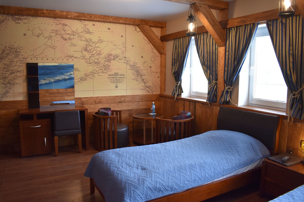 Una habitación de madera con una cama, un escritorio, una silla, una mesita y un mapa en la pared.