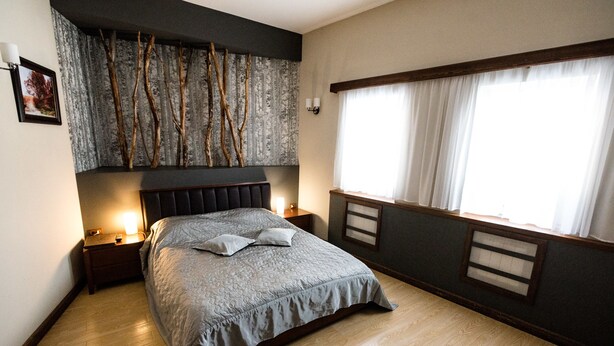 A neatly arranged bedroom with a large bed, a nightstand, a wall-mounted light, and a window with curtains. - Nachalnik Kamchatki (Petropavlovsk-Kamchatskiy)