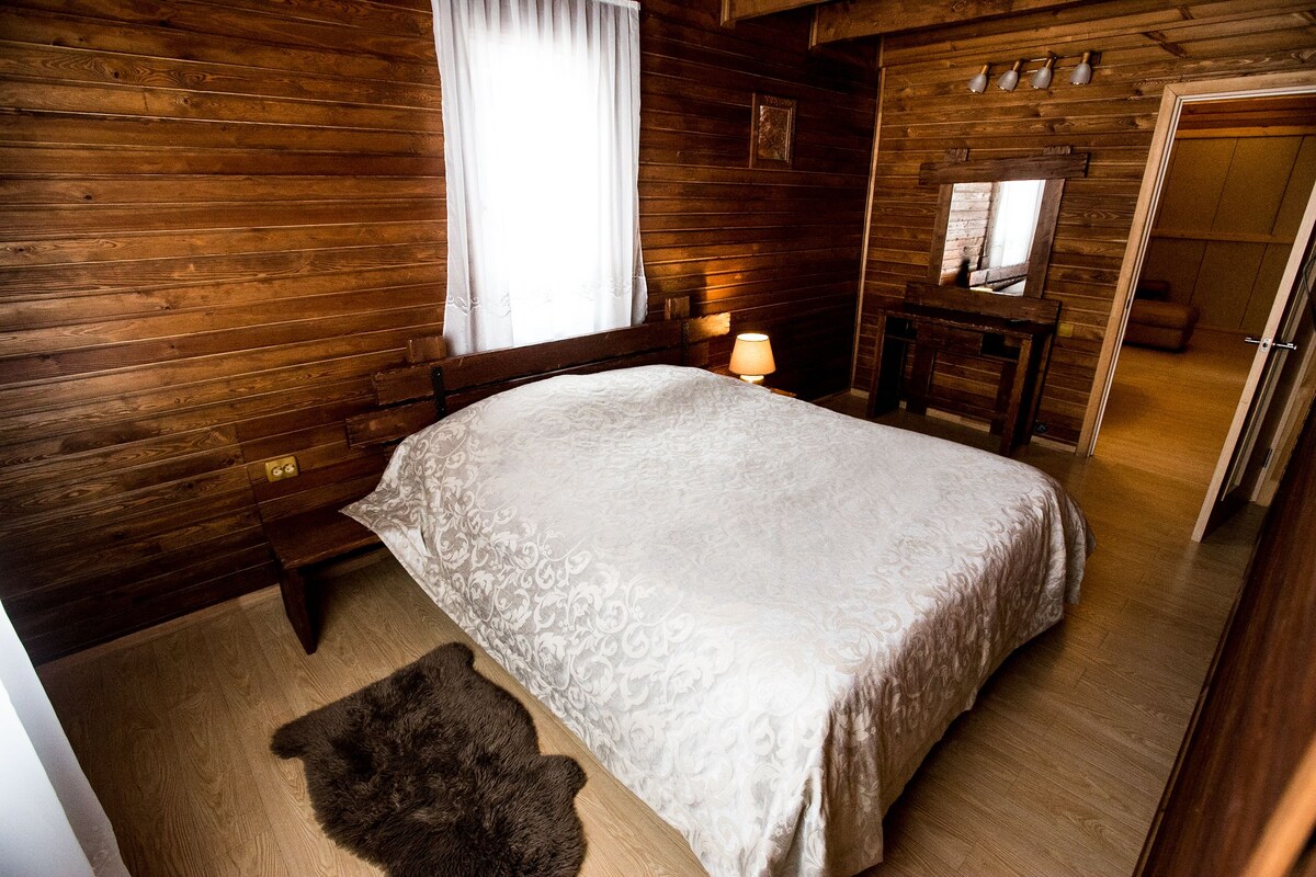 Un dormitorio de cabaña de madera con una cama, una mesita de noche, un espejo y suelo de madera.