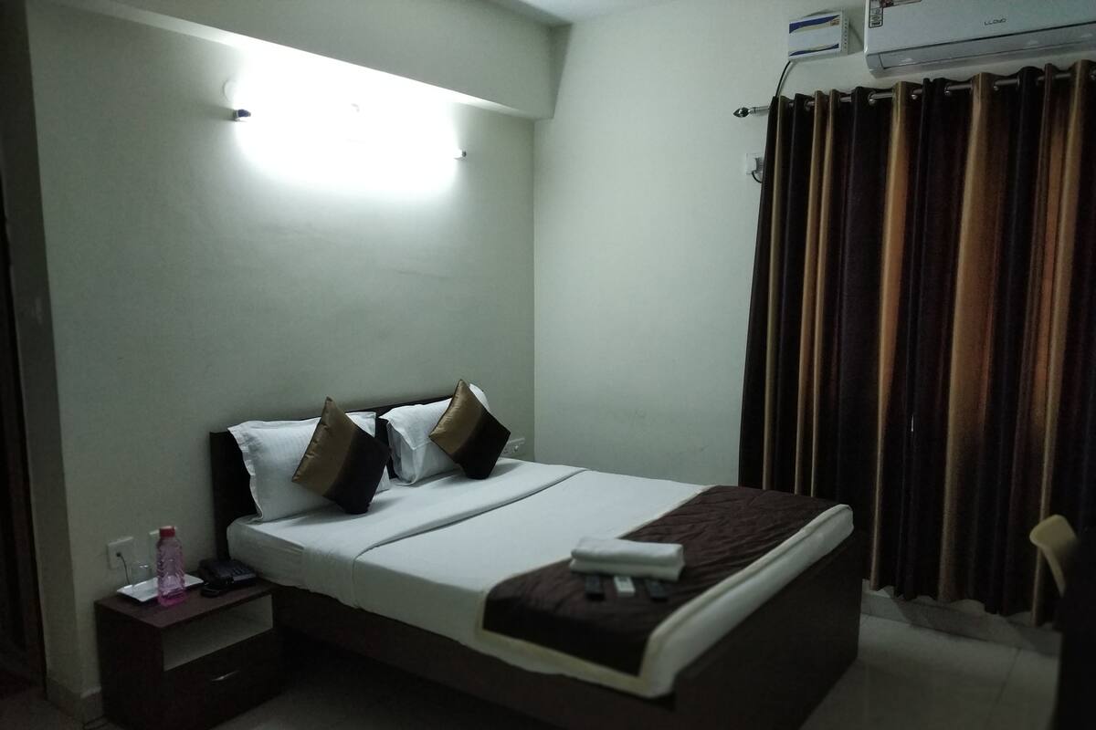 A neatly made bed with pillows, a bedside table with a bottle, and a wall-mounted air conditioner.