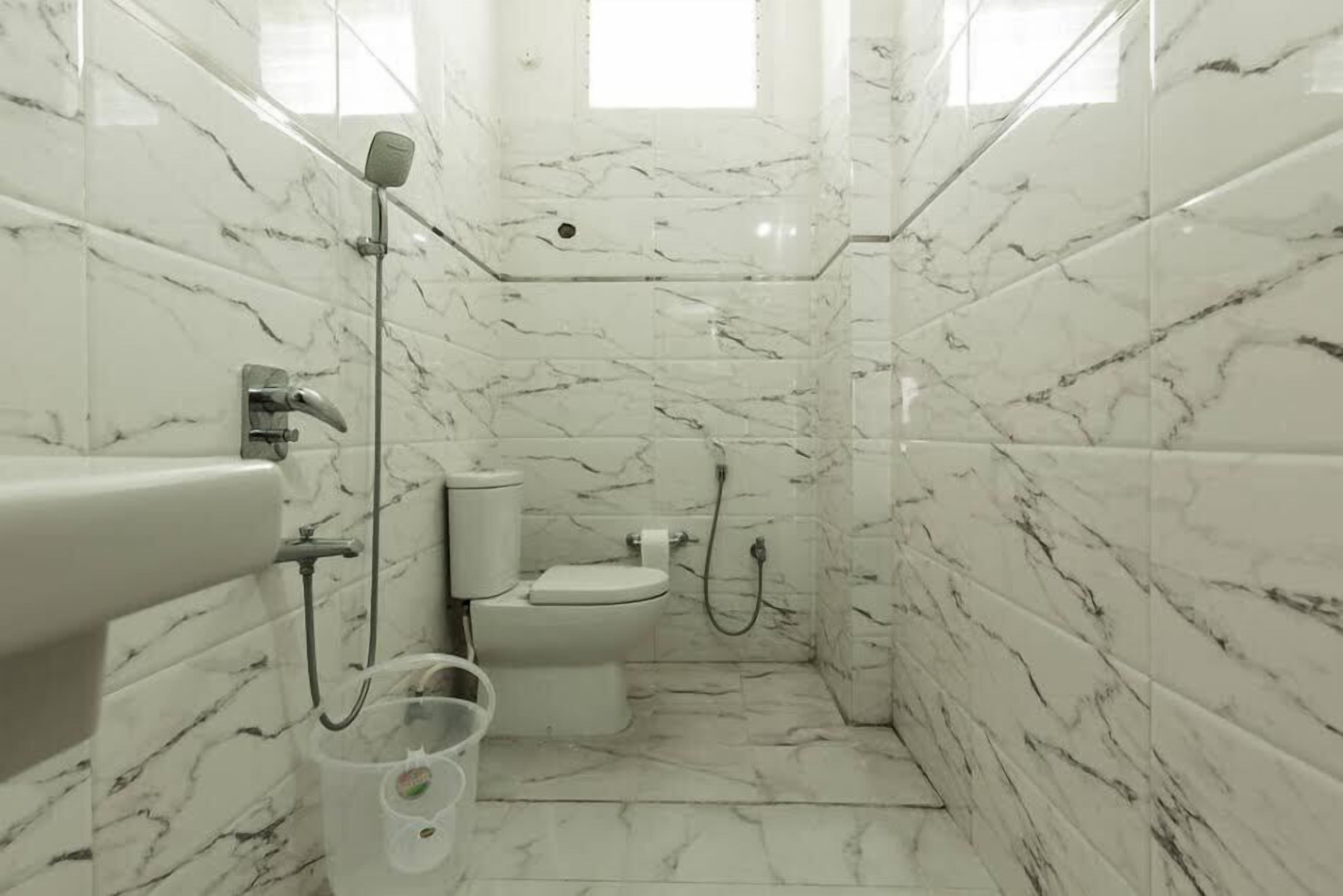 A bathroom with marble walls and floor, a toilet, a sink, and a shower.
