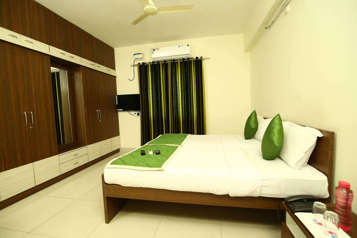 A hotel room with a bed, a green mat, a ceiling fan, and a TV.