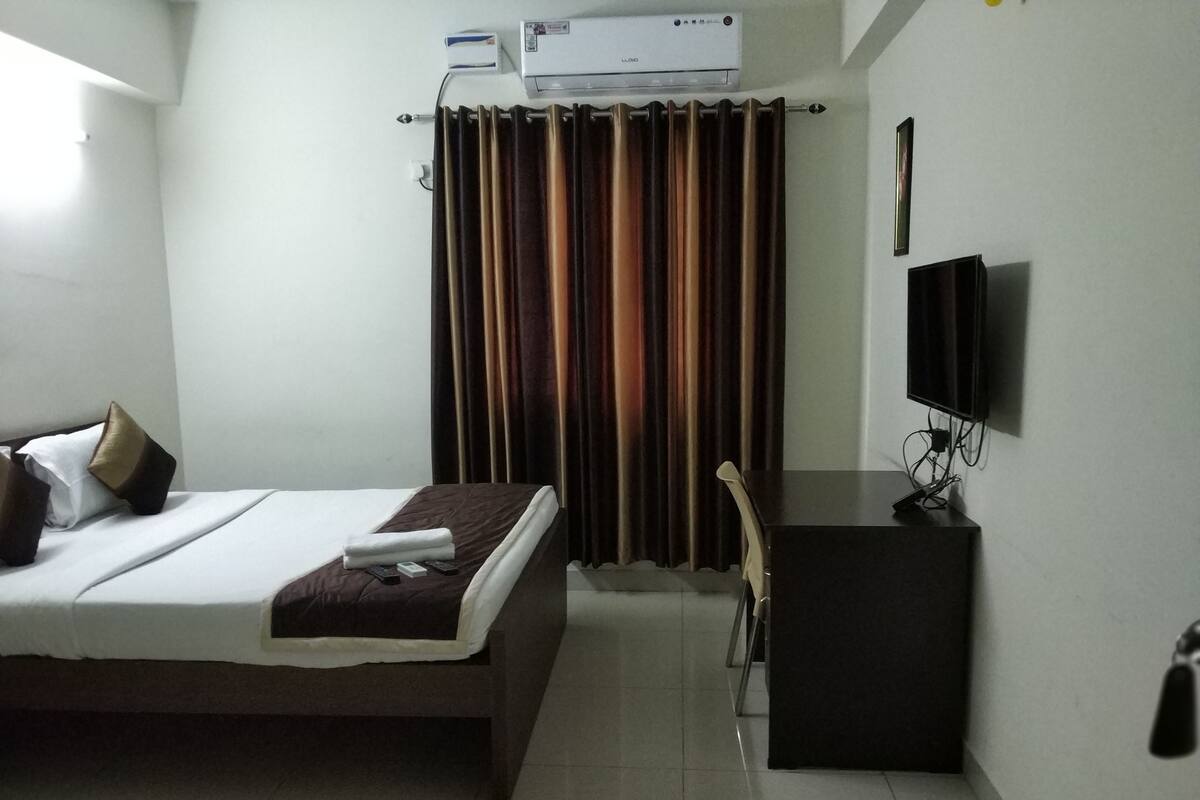 A hotel room with a bed, a desk, a television, and an air conditioning unit.
