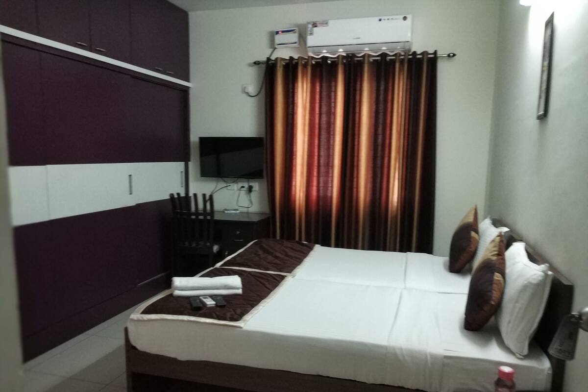 A small, compact room with a bed, a desk, an air conditioning unit, and a curtain.