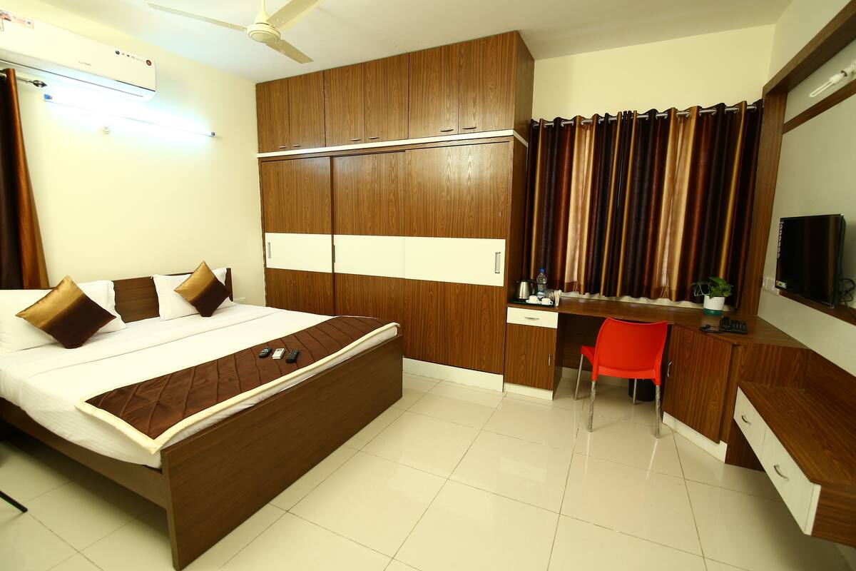 A hotel room with a bed, desk, chair, wardrobe, and a television.