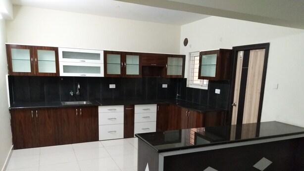 A modern kitchen with dark wooden cabinets, white drawers, and a black countertop. - Fresh Living Prime Hi Tech (Hyderabad)
