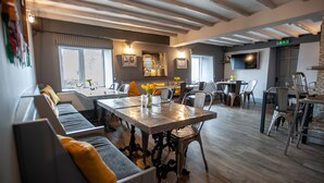 A spacious dining area with a long table, multiple chairs, and a sofa with yellow cushions. - The Slate (Bangor)