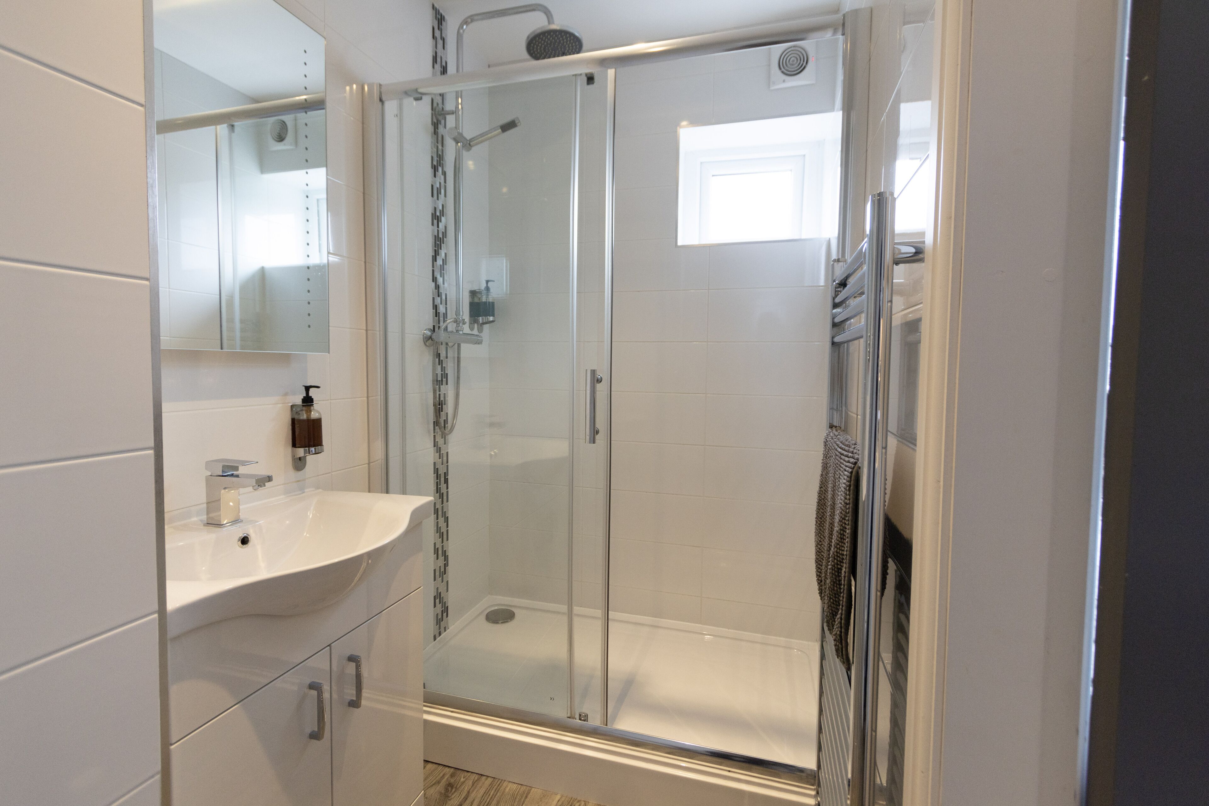 A modern bathroom with a glass-enclosed shower, a white sink, and a mirror.