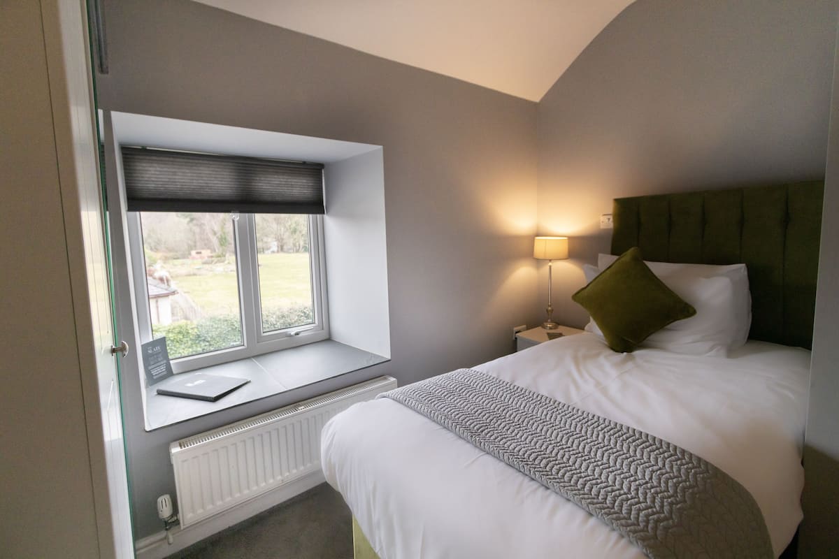 A bedroom with a window seat, a bed with a green pillow, a bedside lamp, and a radiator.