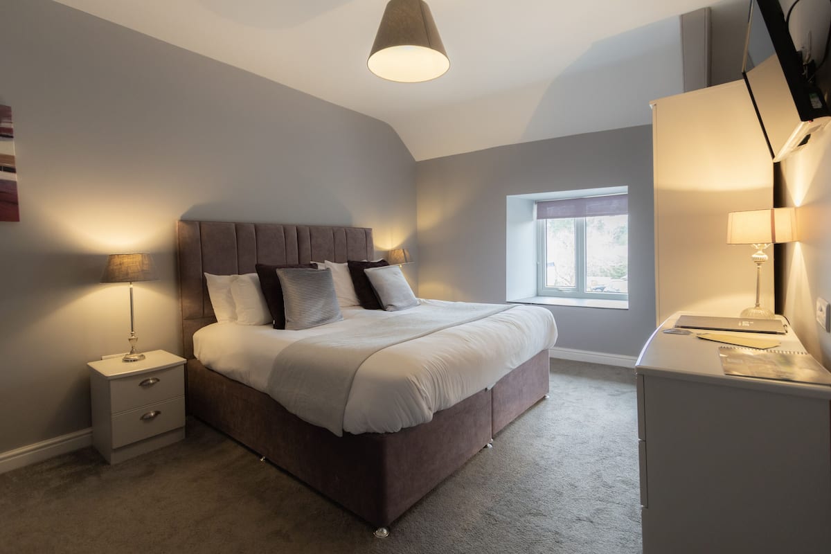 A bedroom with a bed, bedside tables, a desk, and a window.