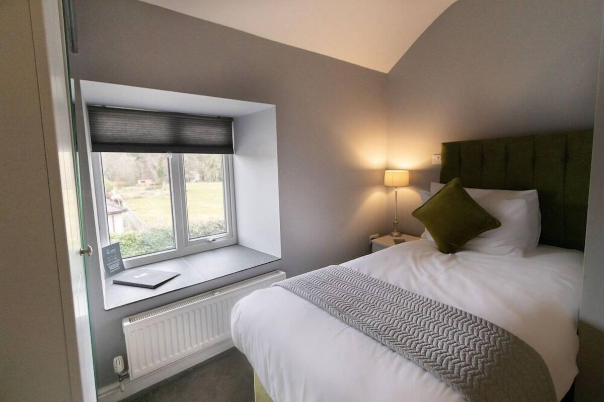 A bedroom with a window seat, a bed with a headboard, a bedside lamp, and a radiator.