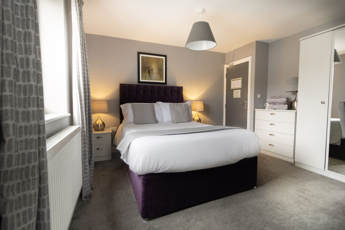 A bedroom with a large bed, bedside lamps, a dresser, and a wardrobe.