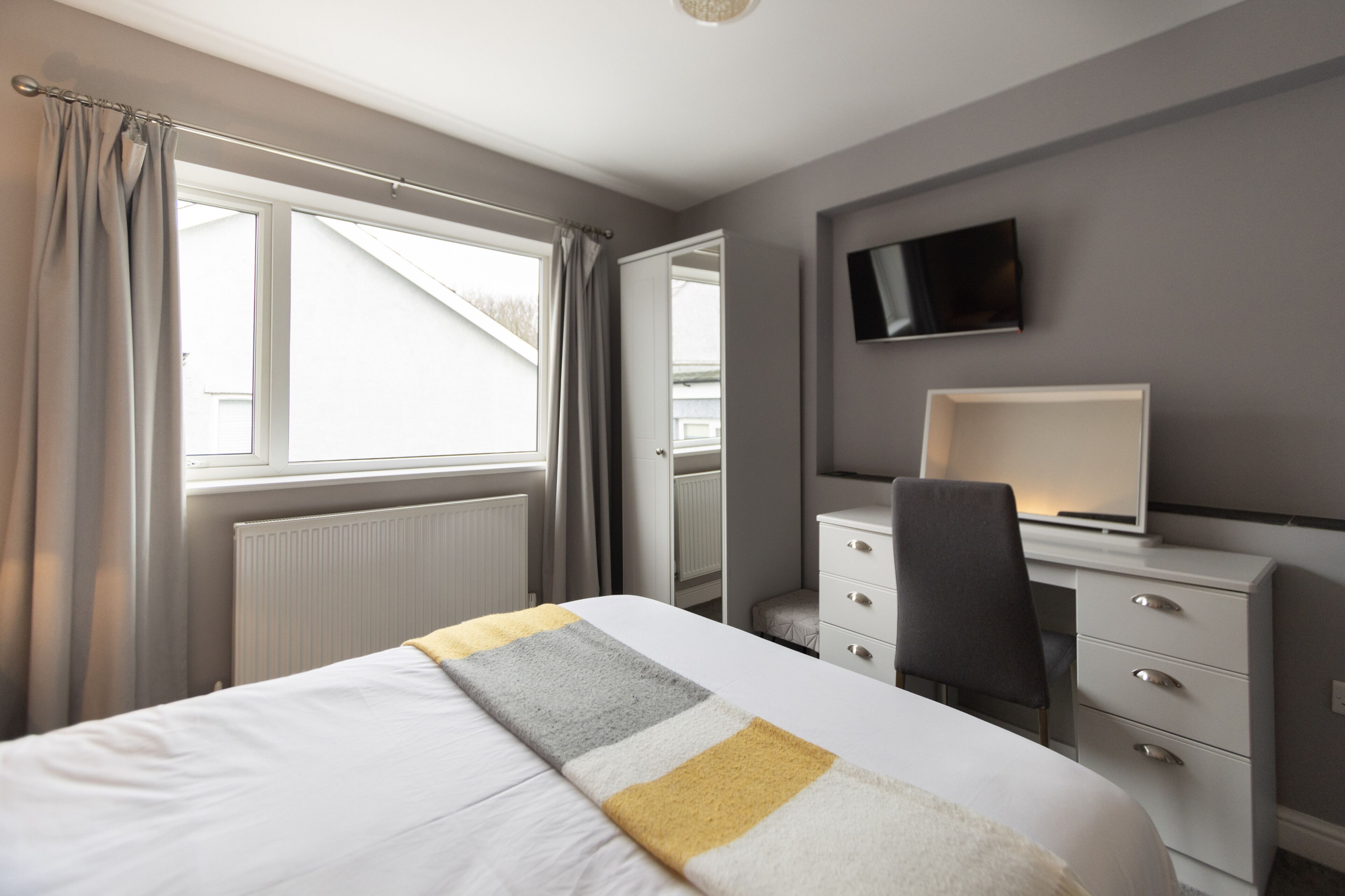 Una habitación de hotel con cama, escritorio, silla, televisor y ventana con cortinas.